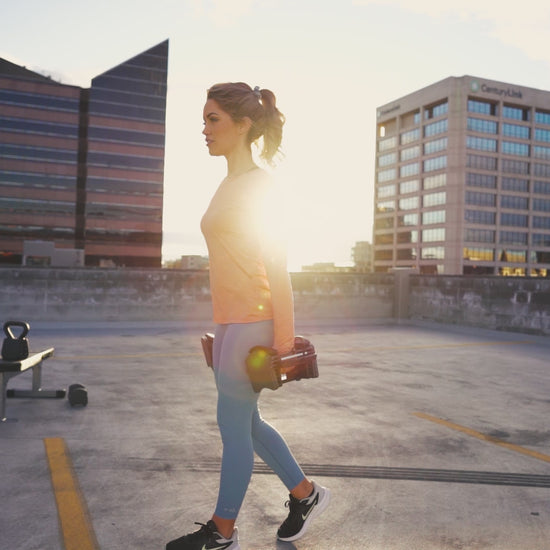 Woman exercising on parking garage rooftop with Powerblock sport 24 adjustable dumbbells.