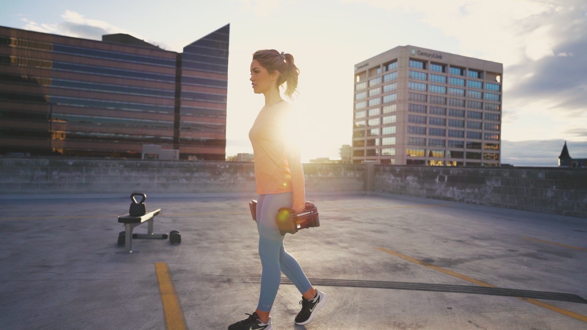 Woman exercising on parking garage rooftop with Powerblock sport 24 adjustable dumbbells.