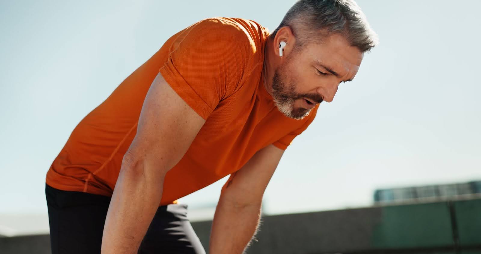 A man in an orange shirt catching his breath while running.