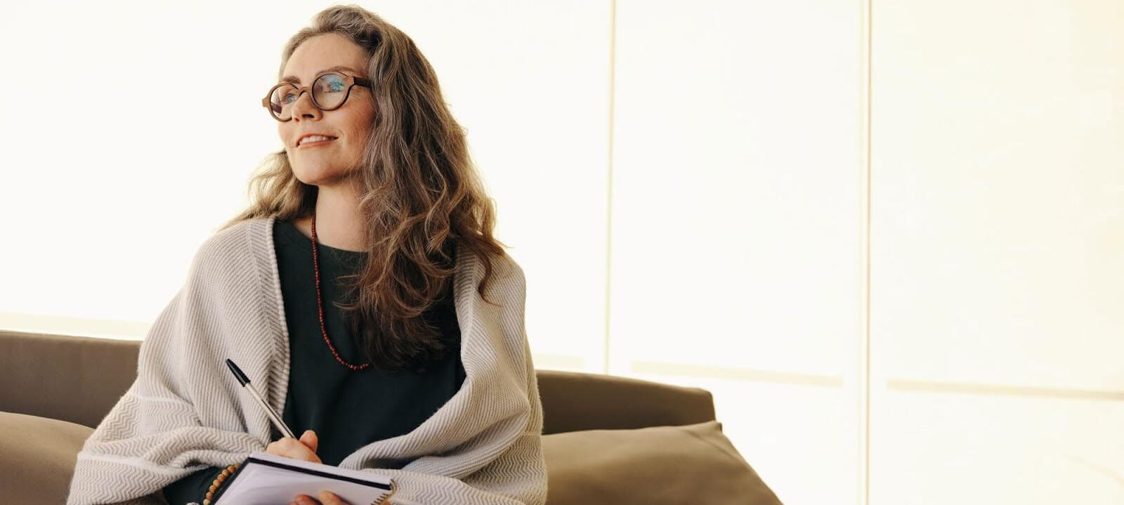 A woman in glasses holding a pen and smiling.